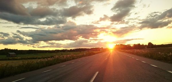 Road by landscape against sky during sunset