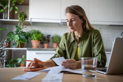 Financial literacy. focused woman using phone calculating expenses trying to analyze domestic budget