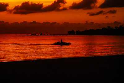 Silhouette people in boat on sea against orange sky