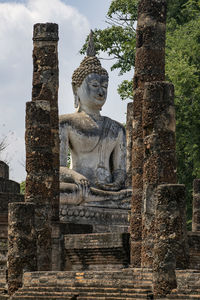 Ruined buddha statue and columns against sky
