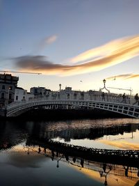 Bridge over river by buildings against sky during sunset