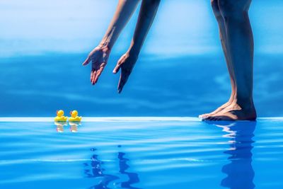 Low section of standing by swimming pool with rubber ducks