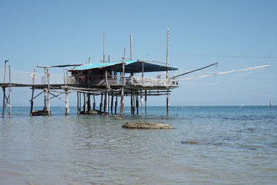 Stilt structure in calm sea against clear sky