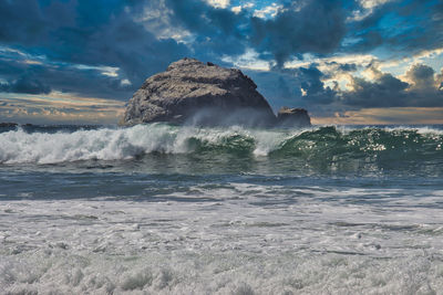 Sea waves splashing on rocks against sky