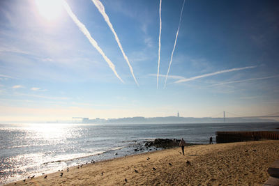 Scenic view of beach against vapor trails in sky