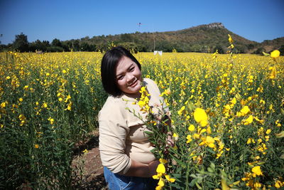 Smiling young woman standing by yellow flowers on field