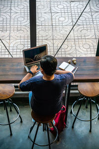 Rear view of man using phone while sitting on table