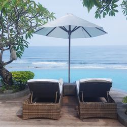 Lounge chairs by swimming pool at beach against sky