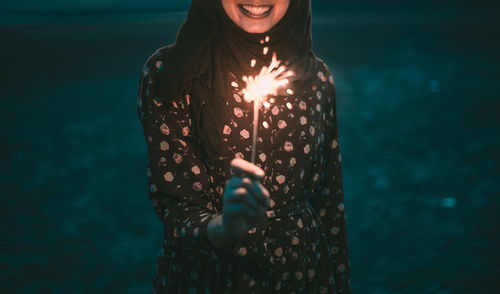 Midsection of smiling woman holding lit sparkler at night