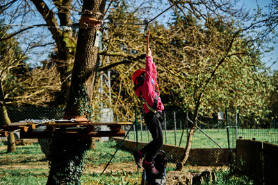 Little girl with protections practicing climbing between trees with ropes and nets