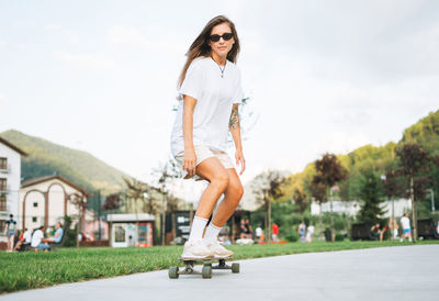 Slim young woman with long blonde hair in light sports clothes on longboard in outdoor skatepark 