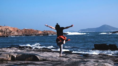 Full length of man dancing on rocks at beach against sky