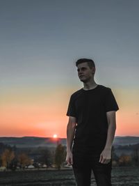 Young man standing against sky during sunset