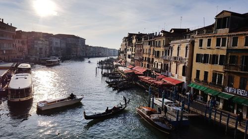 Sailboats moored on canal amidst buildings in city against sky