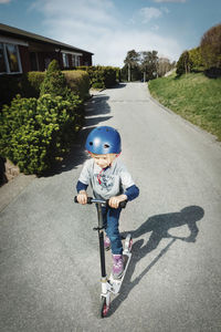 Full length of girl riding push scooter on footpath at yard