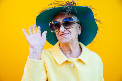 Portrait of senior woman gesturing against yellow background