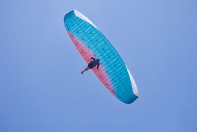 Low angle view of person kiteboarding against clear blue sky