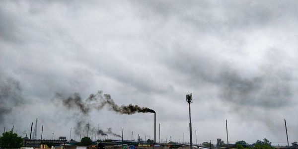 Smoke emitting from factory against cloudy sky