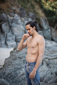 Young man looking away while standing on rock