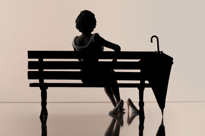 Rear view of woman sitting on bench against wall