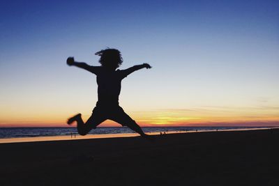Silhouette woman jumping on beach against sky during sunset