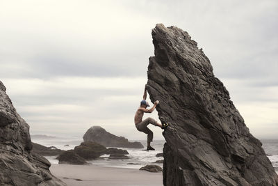 Side view of man climbing rock formation at beach