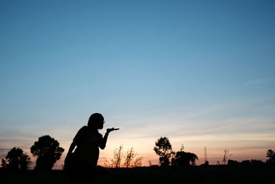 Silhouette man photographing on field against sky during sunset
