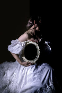 Portrait of young woman standing against black background