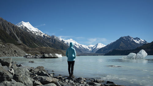 Tourist standing on the shore of tasman glacier terminal lake looking at snow-capped mountains