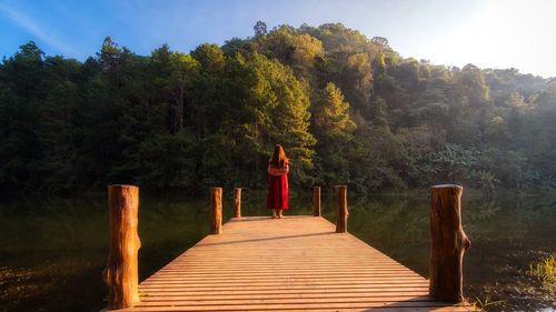 Rear view of woman standing on pier over lake against trees