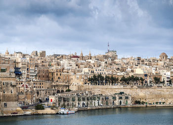 Buildings by river against sky in city