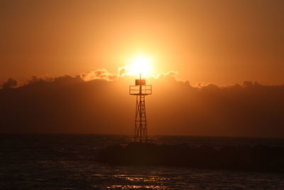 Silhouette lighthouse by sea against sky during sunset