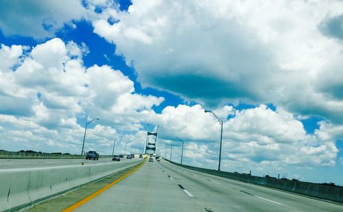 Road passing through highway against cloudy sky
