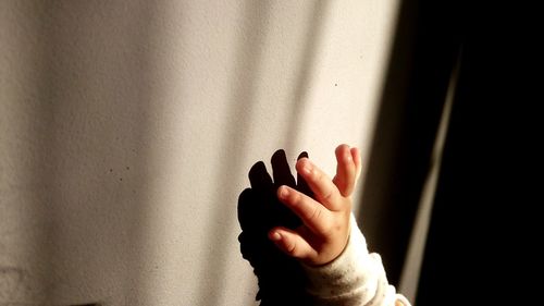 Cropped hand of baby girl by wall with shadow
