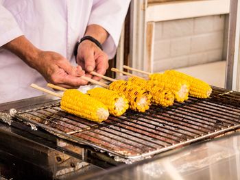 Midsection of man cooking sweetcorns on barbecue grill