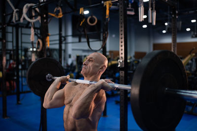 Strong senior man lifting barbell in gym