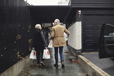 Rear view of senior couple with bags walking together on sidewalk during winter