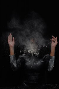 Midsection of man with arms raised against black background