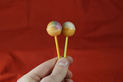 Cropped hand holding lollipop against red fabric