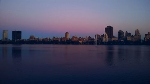 Illuminated cityscape by sea against sky at dusk