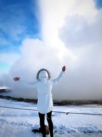 Full length of woman with arms outstretched standing on snow covered field against cloudy sky