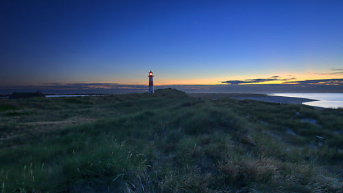 Lighthouse on field against sky during sunset