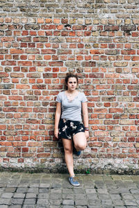 Woman looking away while leaning on brick wall