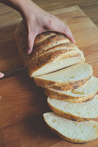 Cropped hand cutting bread on wooden table