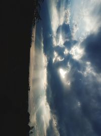 Low angle view of sunlight streaming through storm clouds