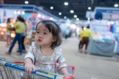 Baby girl sitting in shopping cart at supermarket