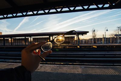 Cropped image of hand holding eyeglass at railroad station