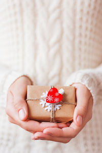 Woman in knitted sweater holds present. gift  with red heart. diy way to pack christmas presents. 