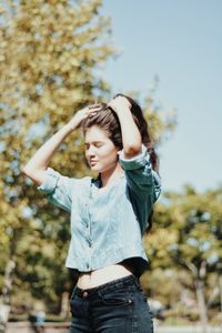 Young woman standing against trees during sunny day