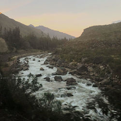 Scenic view of river amidst mountains against sky during sunset